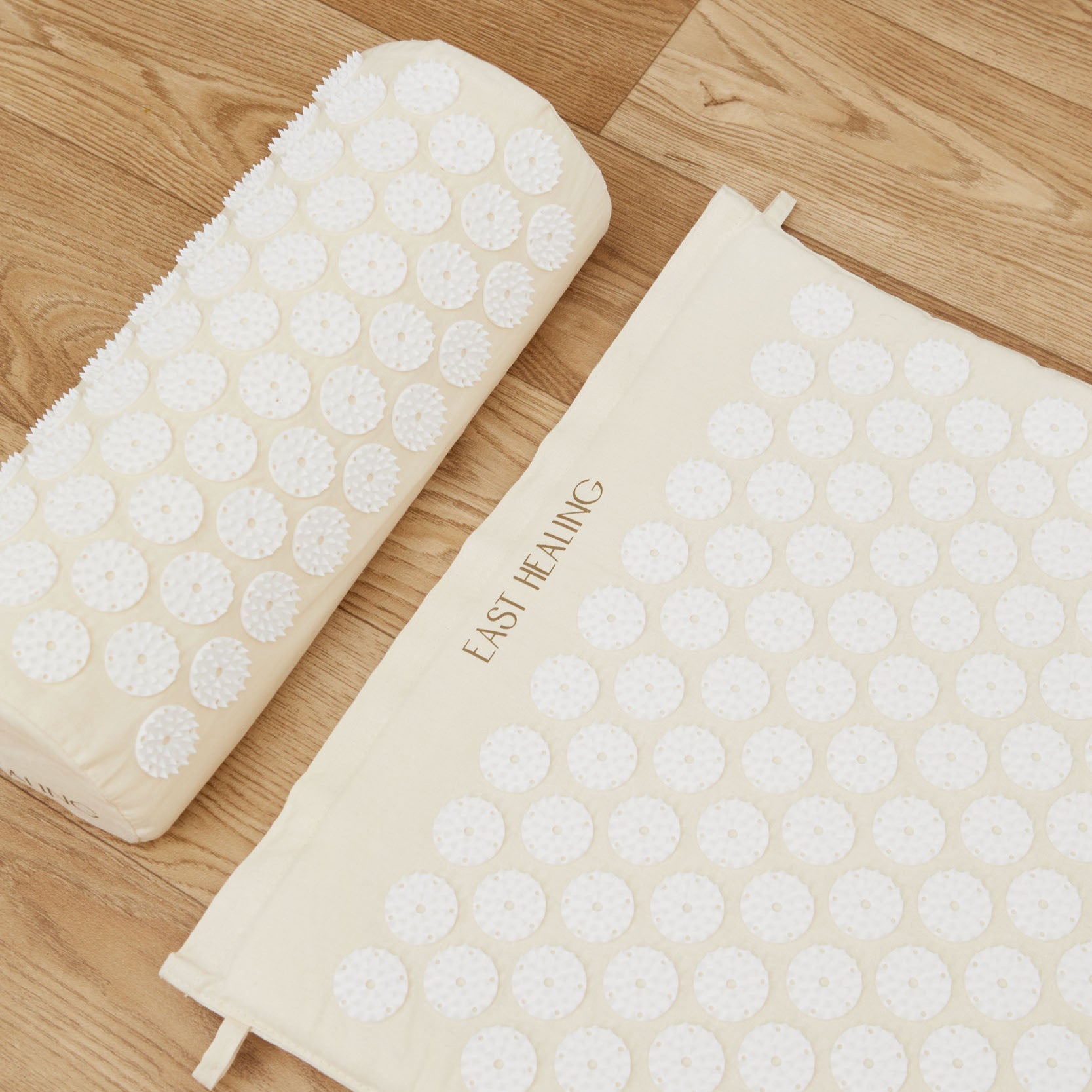 An acupressure mat and pillow with a textured surface designed for relaxation and stress relief, placed on a wooden floor.